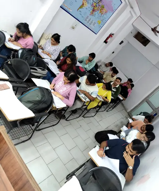 Students at desks in the second classroom, writing with a wall map behind them